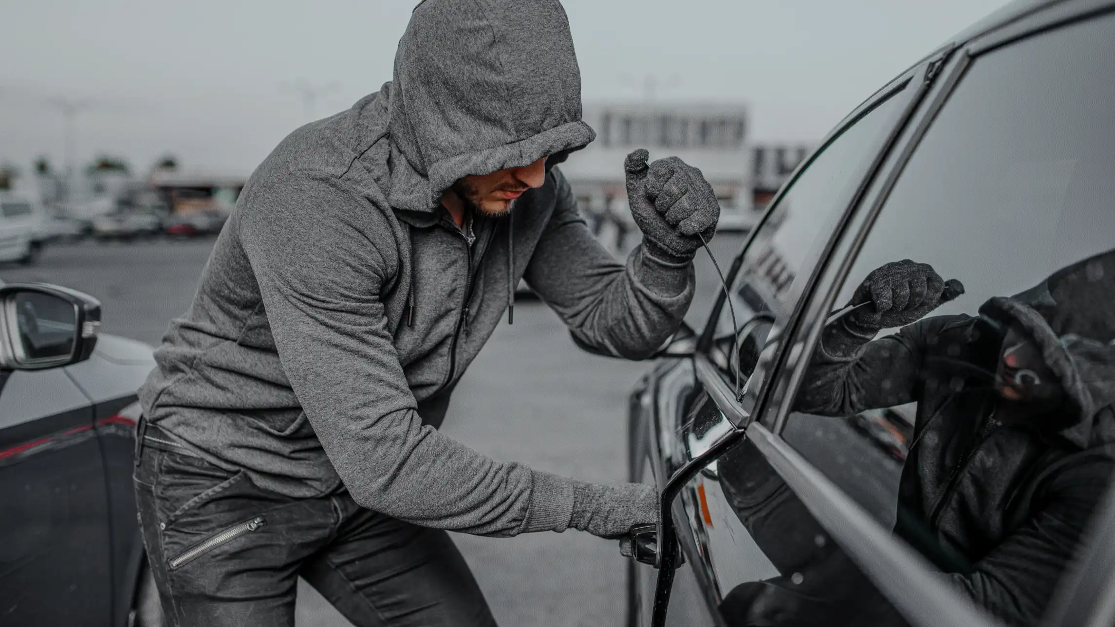 Hooded man breaking into car in parking lot