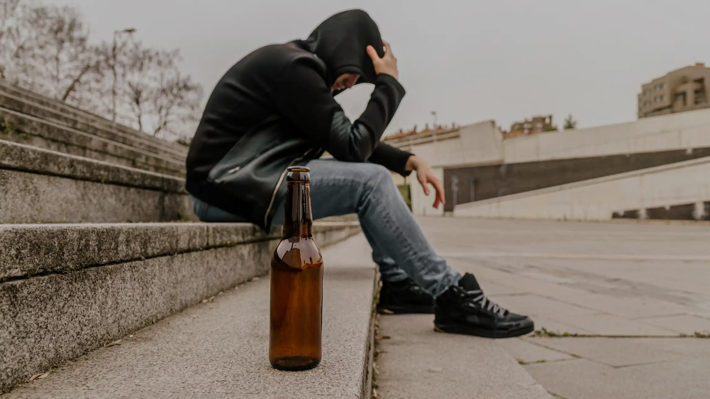 Person hiding in a hoodie drinking from beer bottle on the street
