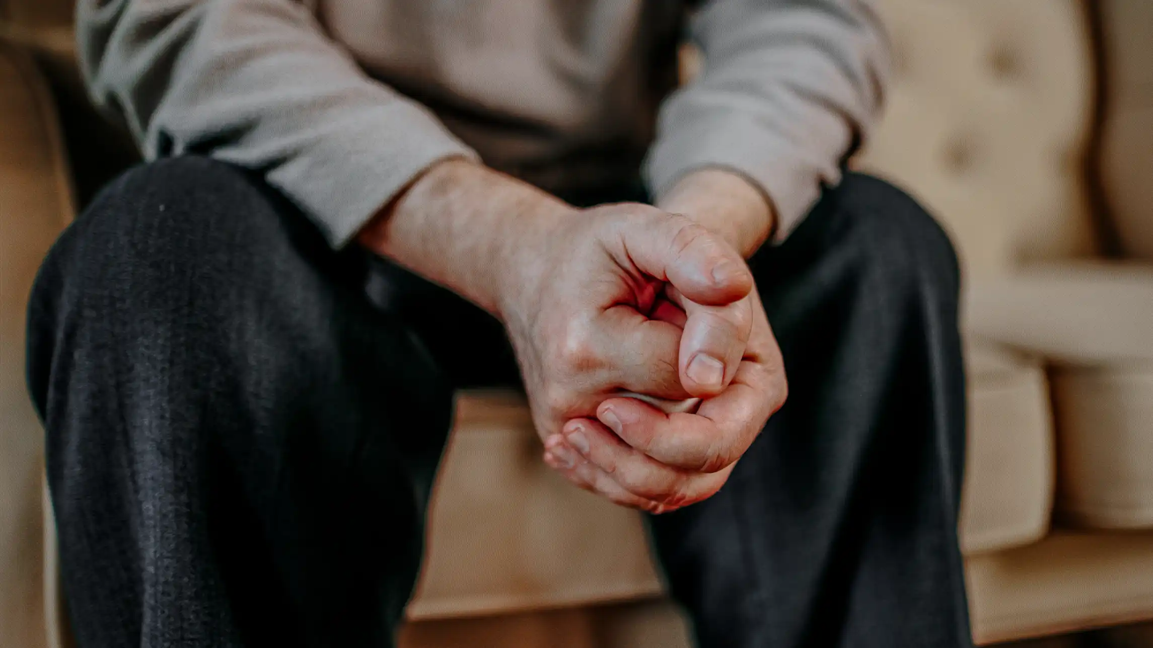 Worried person sitting on couch with clasped hands