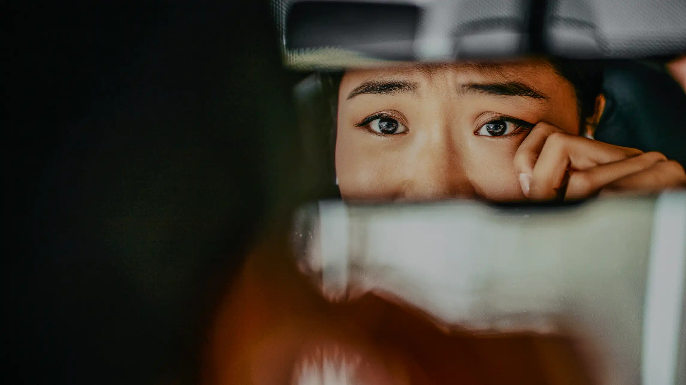 Woman wiping tears in car mirror