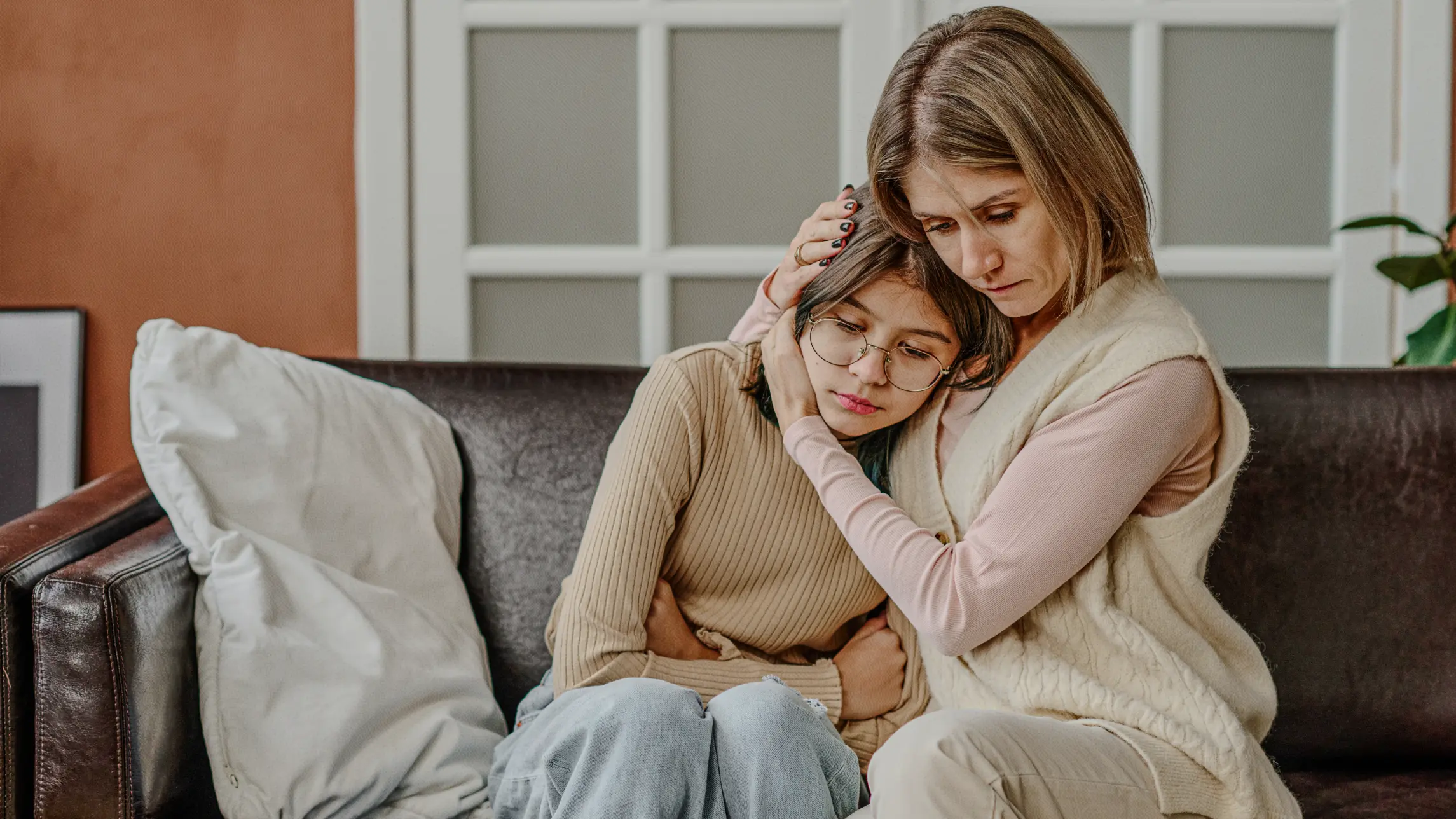 Woman embracing sad child on couch