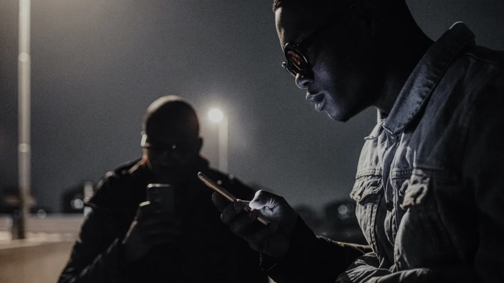 Men waiting in the dark under streetlights on their phones