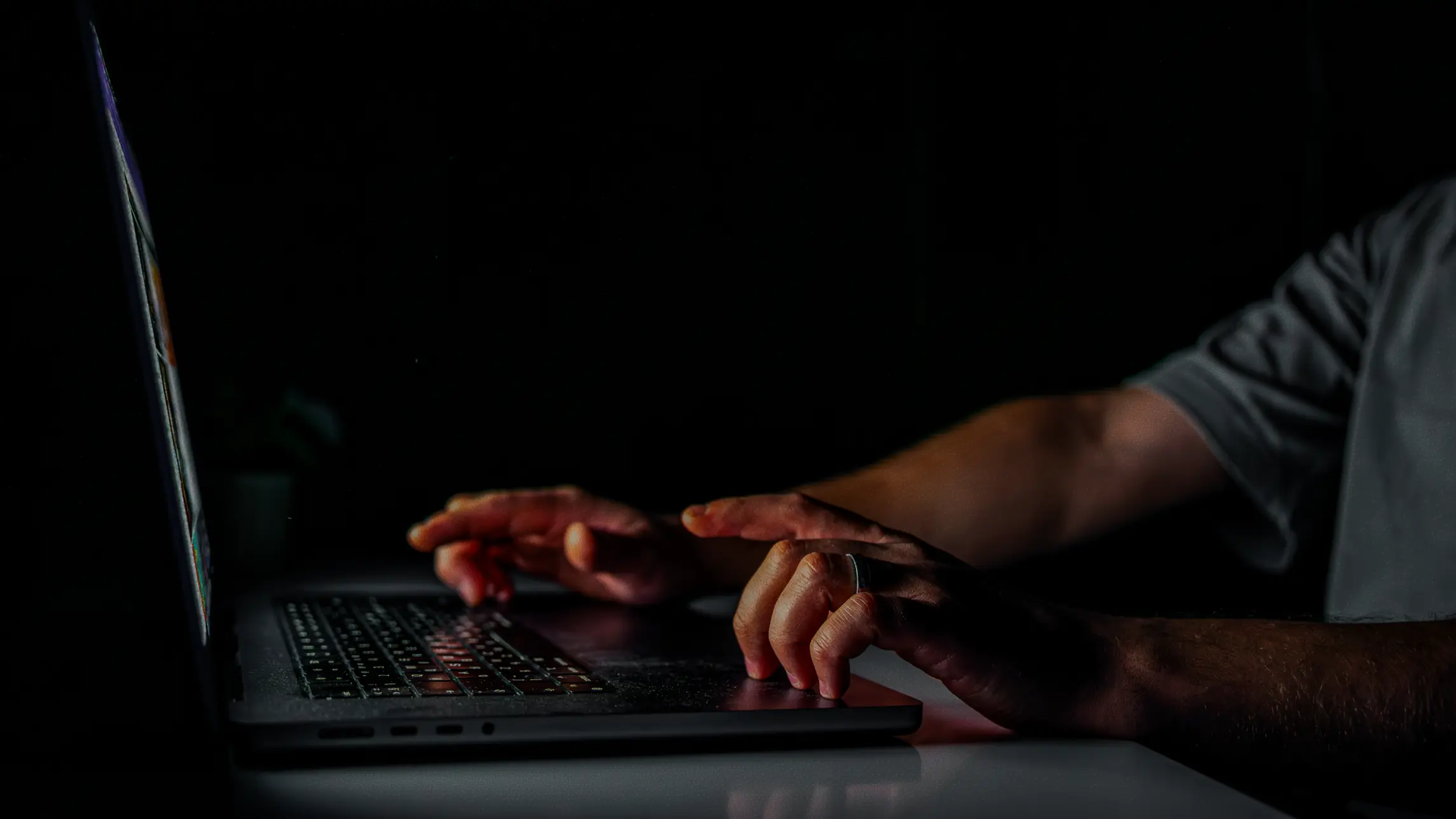 Hands in the dark typing in the light of a laptop screen
