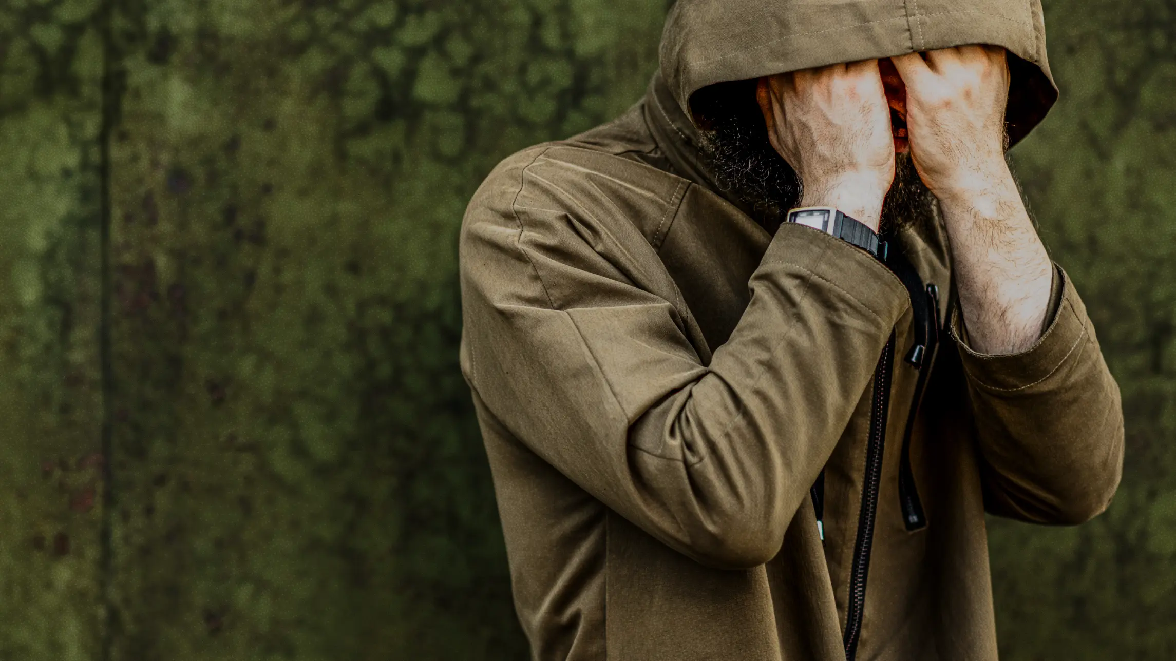 Man hiding face with both hands wearing zipped up jacket with hood up