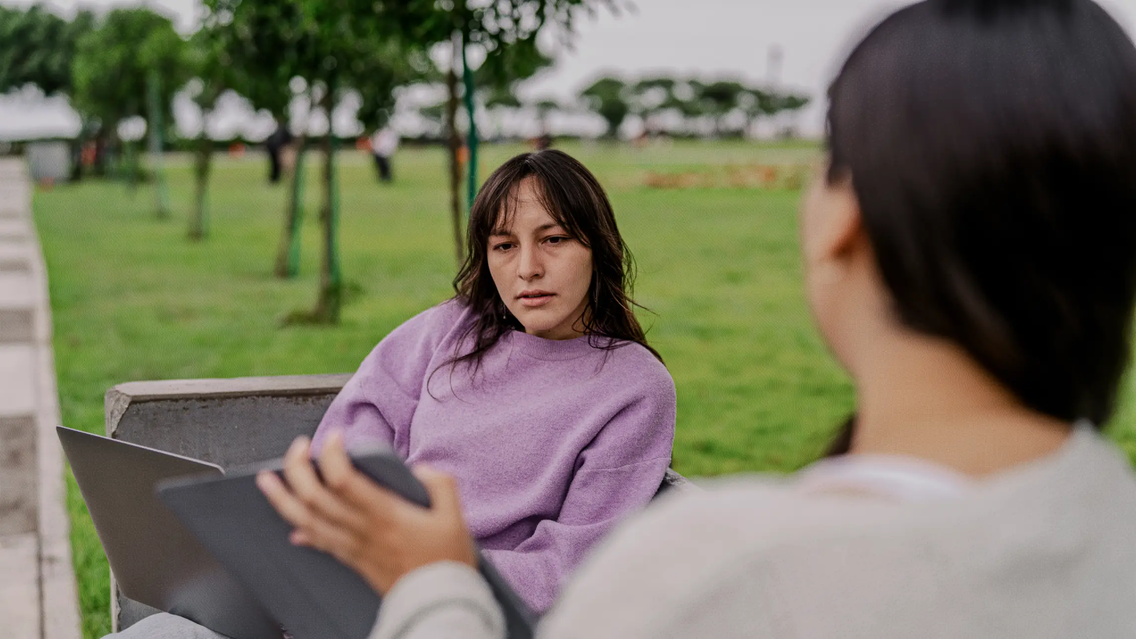 Women on a park bench looking at laptops
